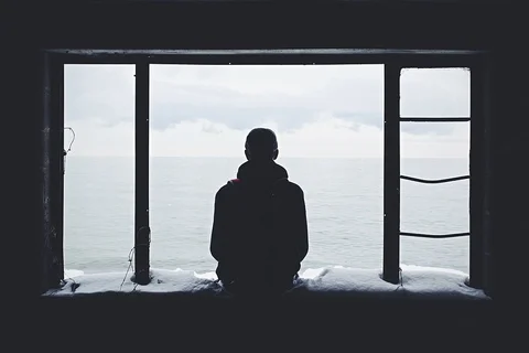 Solitary person silhouetted beside a window